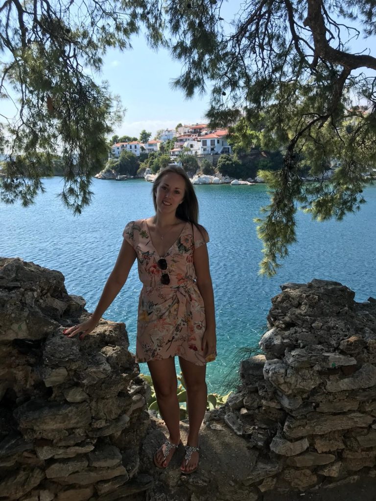 Charlotte Haines Staff Spotlight feature photograph. Charlotte stands near the seaside on holiday on a summer's day.