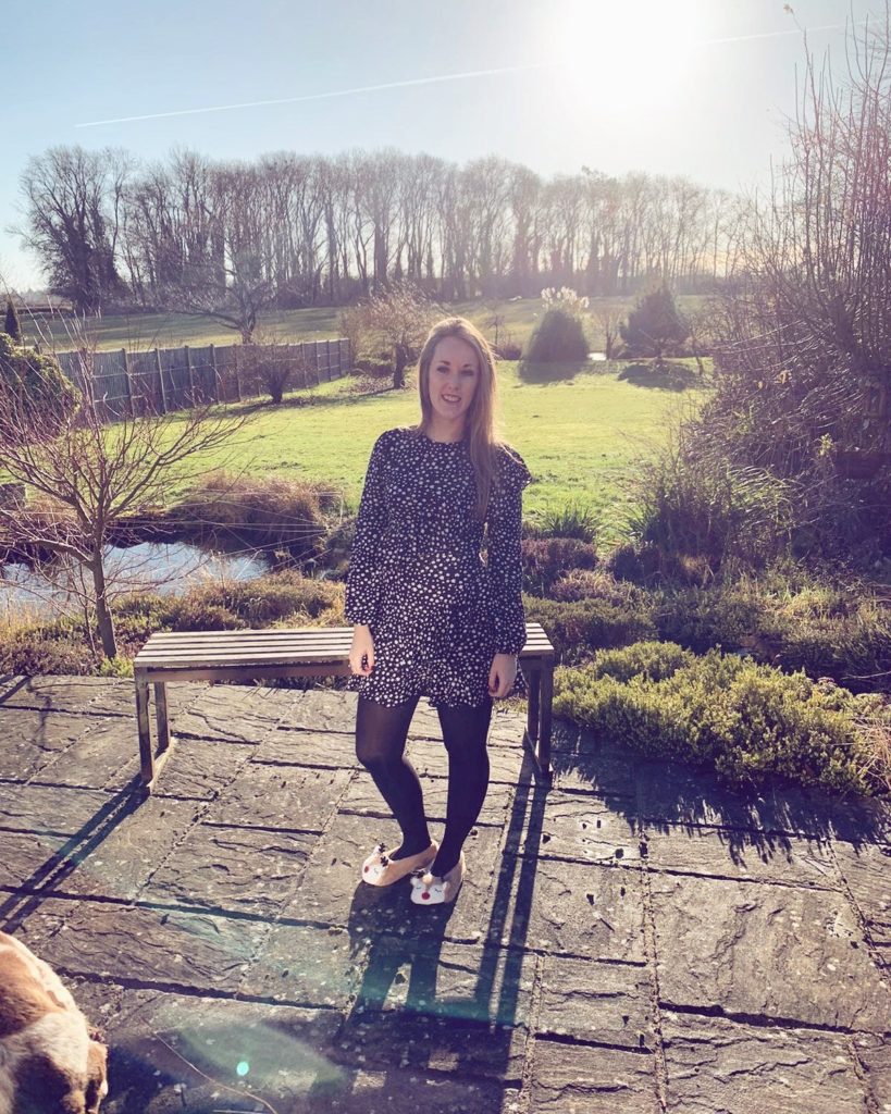 Charlotte Haines Staff Spotlight feature photograph. Charlotte stands on decking in a beautiful garden on a winter's day. 